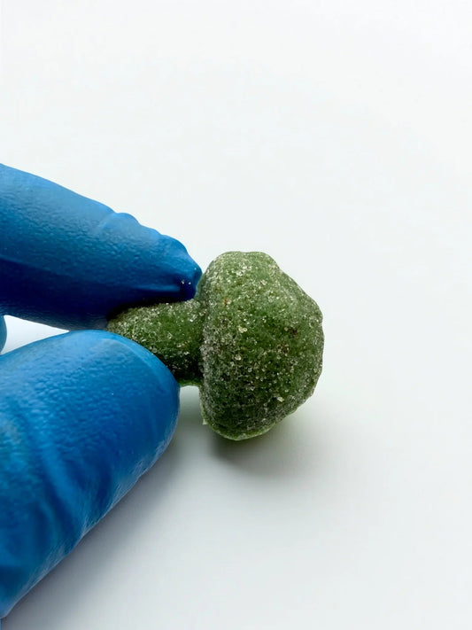 Green textured 'Stoner Mushroom Gummies' edible (30 gummies, 350mg ea | 10500 mg Total), as seen at StewartHemp.com held by blue-gloved hands on a white background
